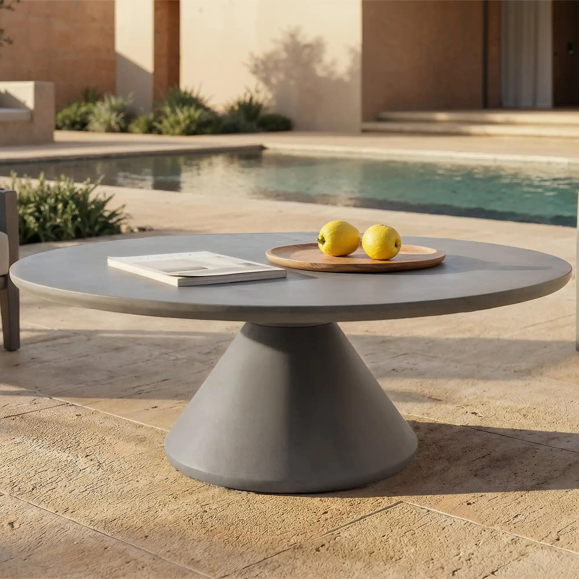 Table basse ronde en béton design au pied conique installée près d'une piscine, avec un plateau en bois et un livre